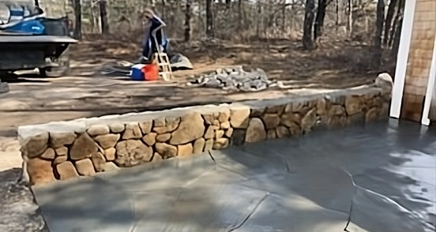 Picturesque driveway and retaining wall at a charming house in Wellfleet, Massachusetts, lined with natural stone and bordered by well-maintained landscaping.